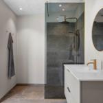 Moderne Dusche mit Glaswand, Waschtisch mit Spiegel und Handtuchhalter an der Wand.