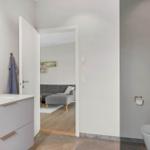 Badezimmer mit Waschtisch und Toilette, Blick in Wohnbereich mit Sofa.