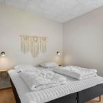 Schlafzimmer mit Doppelbett, weißen Bettwäsche und Holzfußboden. An der Wand hängt ein Macramé-Teppich.