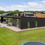 Moderne Villa mit Holzterrasse und Garten. Mehrere Gebäude im Hintergrund.