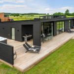 Moderne Villa mit großem Holzdeck, Whirlpool, Grill und Loungebereich. Blick auf grüne Landschaft.