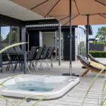 Outdoor area with hot tub, umbrella, and lounge chairs on wooden deck.