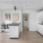 Kitchen with dining area, white cabinets, and wooden floor. Hallway to the apartment.
