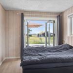Bedroom with view of garden and terrace. Wooden walls and large windows.