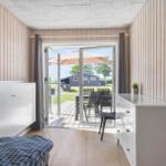 Bedroom with view of terrace and garden. Wooden walls, white furniture, and sliding door.