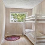 Room with bunk bed, wood-paneled walls, and window with view of trees.