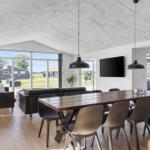 Dining area with wooden table and chairs. In the background, a living area with sofa and large window.
