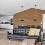 Living and dining area with black leather sofa and wooden wall. Kitchen in background.