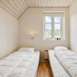 Zwei Betten mit weißen Bettwäsche, Fenster und Wandlampe in einem Raum mit Holzboden.