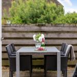 Terrasse mit Tisch, Stühlen, Blumen und einer Flasche Sekt.