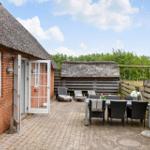Haus mit strohgedecktem Dach, Terrasse mit Tisch, Stühlen und Liegestühlen.