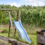 Holzspielplatz mit Rutsche und Schaukel im Grünbereich.
