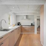 Modern kitchen with wooden floor and light cabinets. Window, sink, and range hood visible.