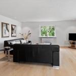 Living room with black leather sofa, wooden floor, and window with view of trees.