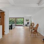 Entrance area with white walls, wooden floor, and seating. Corridor to living room with garden view.