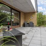 Terrace with seating and table. Background: house wall with glass tiles and green areas.