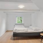 Bedroom with sloped ceiling, bed, side table, and window with view of trees.
