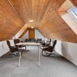 Attic room with wooden ceiling, table, four chairs, and sofa. Large skylight.
