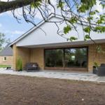Modern villa with terrace, seating, and glass front. View of garden and sky.