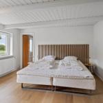 Bedroom with double bed, wooden floor, and window with view of green area.