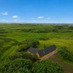 A yellow house with a black roof is situated in a green landscape with meadows and trees.