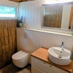 Badezimmer mit Waschbecken, Spiegel und Toilette unter Holzdecke.