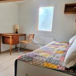 Schlafzimmer mit Bett, Schreibtisch und Fenster. Wandverkleidung und Holzboden.