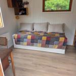 Schlafzimmer mit Bett, Decke und Fenster. Holzfußboden und Wandregale.