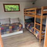 Zimmer mit Etagenbett und Schlafcouch, Holzfußboden und Fenster mit Blick auf Bäume.