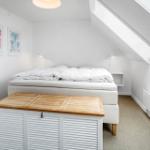 Schlafzimmer mit Dachschrägen, Bett, Holzbox und Wandbildern.
