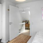 Schlafzimmer mit weißem Schrank, Bett und Tür zu einem Flur mit Holzboden und weißer Brüstung.