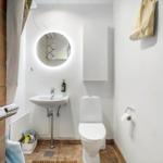 Badezimmer mit Toilette, Waschbecken und runden Spiegel mit Beleuchtung.