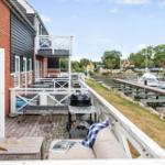 Terrasse mit Grill und Sofa, Blick auf Hafen mit Booten.