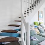 Eine Treppe mit braunen Stufen führt zu einem Wohnbereich mit Sofa und Fenster.