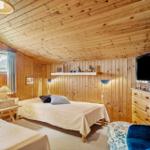Zimmer mit Holzwand und -decke, zwei Betten, Fernseher und blauer Sessel.