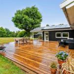Holzterrasse mit Sitzgruppe, Garten und Baum. Schwarzes Haus mit Terrassentüren.
