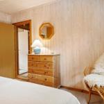 Schlafzimmer mit Holzwand, Bett, Schrank, Stuhl und Spiegel.