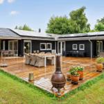 Schwarze Holzhütte mit großem Holzterrasse, Gartenmöbeln und Pflanzen.