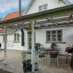 Terrasse mit Tisch, Stühlen, Grill und Pergola unter einem blauen Himmel.