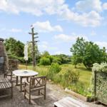 Terrasse mit Holztisch und Stühlen, Blick auf Garten und Baum mit Flagge.