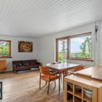 Wohnküche mit Esstisch, Sofa und Kaminofen. Blick auf grüne Landschaft.