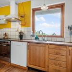 Küche mit Holzschränken, Spüle und Fenster. Gelbe Wand und Edelstahlherd.