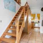 Holztreppe führt zur oberen Etage. Küche mit gelben Wänden und weißen Schränken.