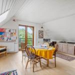 Dachgeschosszimmer mit Esstisch, Sitzgelegenheit und Fenstern. Holzboden und weiße Wände.