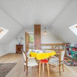 Dachgeschosszimmer mit Tisch, Stühlen und Dachfenstern. Holzboden und Bücherregale.