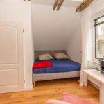 Schlafzimmer mit Bett, Schreibtisch und Fenster. Holzboden und Deckenbalken.