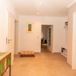 Flur mit Holzboden, Wandbild und Schuhschrank. Links Spiegel und Tisch mit Holzschild.