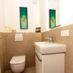 Badezimmer mit Toilette, Waschbecken und Spiegel. Wandbild und Hinweisschild sichtbar.