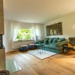 Wohnzimmer mit grünem Sofa, Holzboden und Kamin. Fenster mit Blick auf Garten.