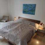 Schlafzimmer mit Bett, Nachttisch und Sessel. Wandbild und Lampen sichtbar.
